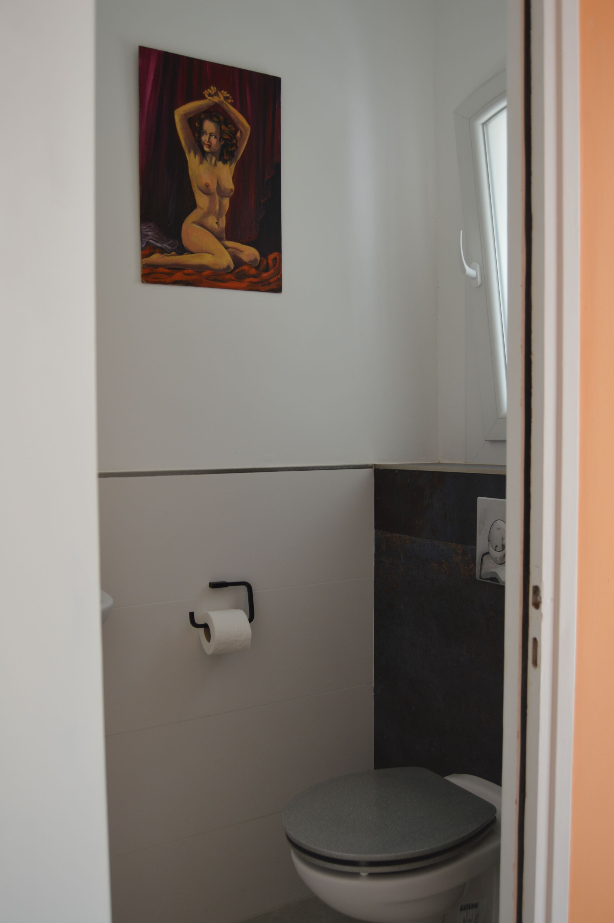 A bathroom with a toilet, a roll of toilet paper, and a painting on the wall.