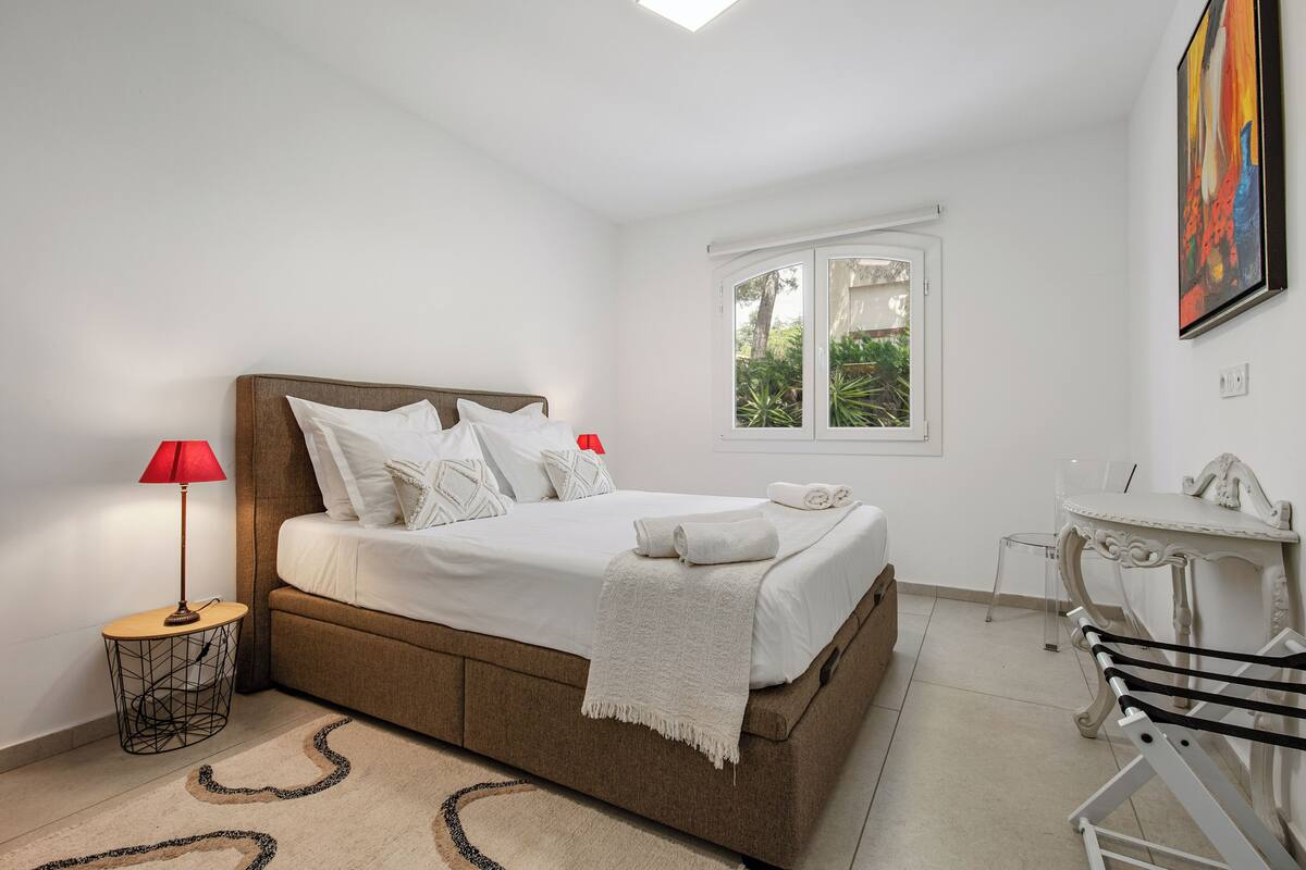 A bedroom with a bed, a desk, a chair, a window, and a lamp.