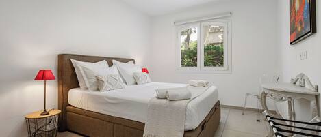 Une chambre à coucher avec un lit, un bureau, une chaise, une fenêtre et une lampe.