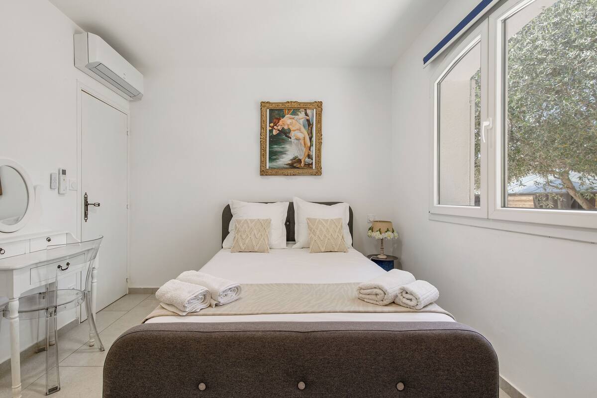 A bedroom with a bed, a bedside table, a mirror, and a window.