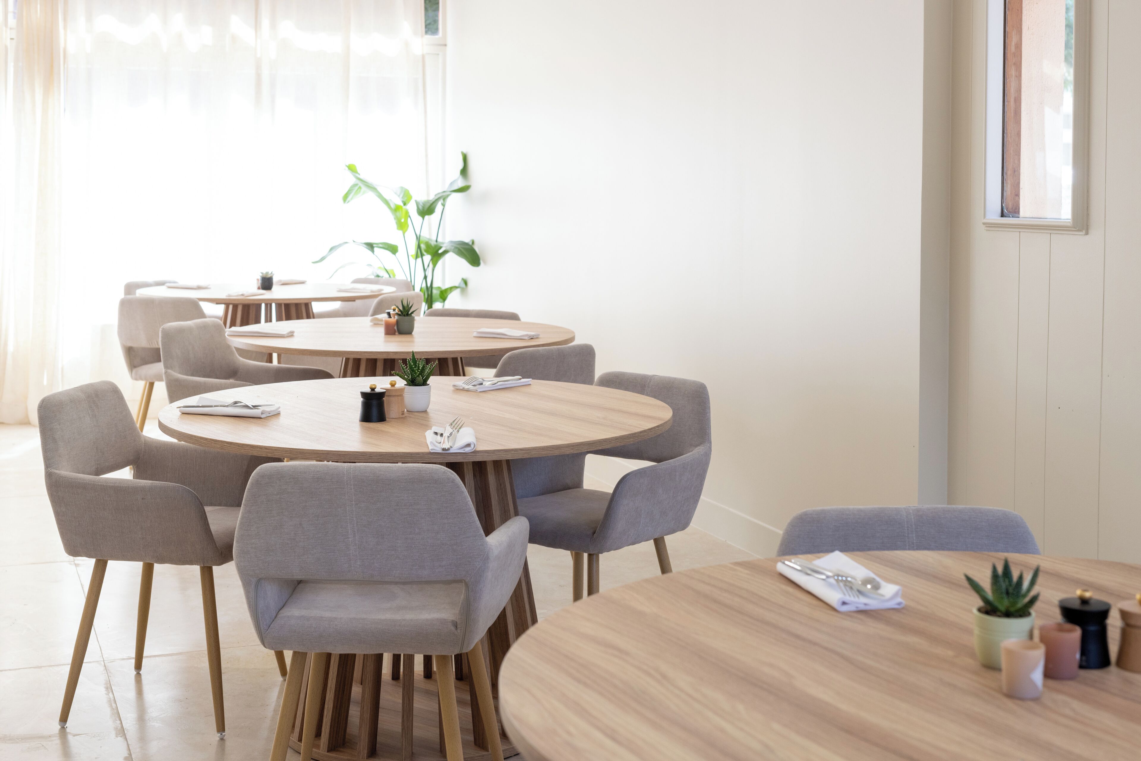 Un comedor moderno con mesas redondas de madera y sillas tapizadas en gris.