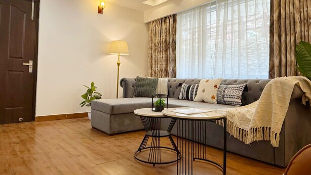 Een moderne woonkamer met een grijze bank, een ronde salontafel en een vloerlamp.