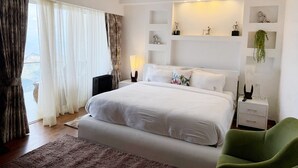 Een moderne slaapkamer met een groot bed, een nachtkastje, een groene fauteuil en uitzicht op het landschap door dunne gordijnen.