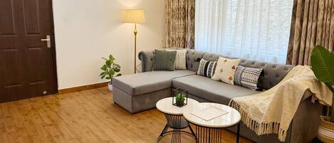A living room with a sectional sofa, a round coffee table, a floor lamp, and a large window with curtains.