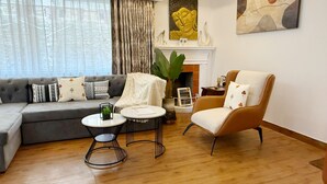 Een moderne woonkamer met een grijze bank, een ronde salontafel, een bruine fauteuil en een open haard.