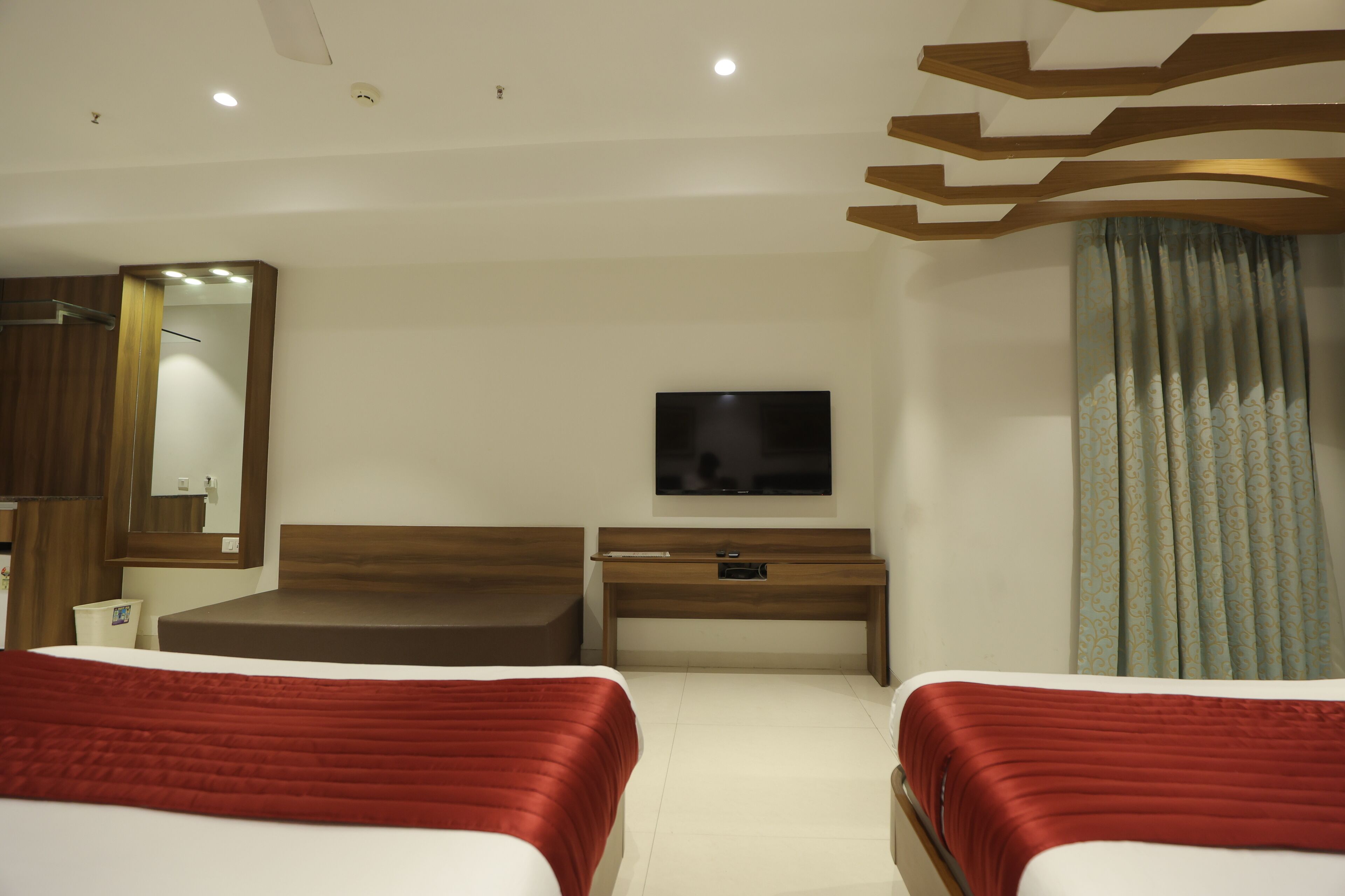 A hotel room with two beds, a TV, a wooden desk, and a mirror.