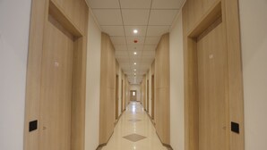 A long, narrow hallway with wooden doors on both sides and a tiled floor. - Hotel Shreeji Vatika-Airport Road (Surat)