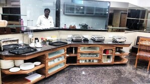 A kitchen with a chef, wooden cabinets, and various kitchen appliances. - Hotel Shreeji Vatika-Airport Road (Surat)