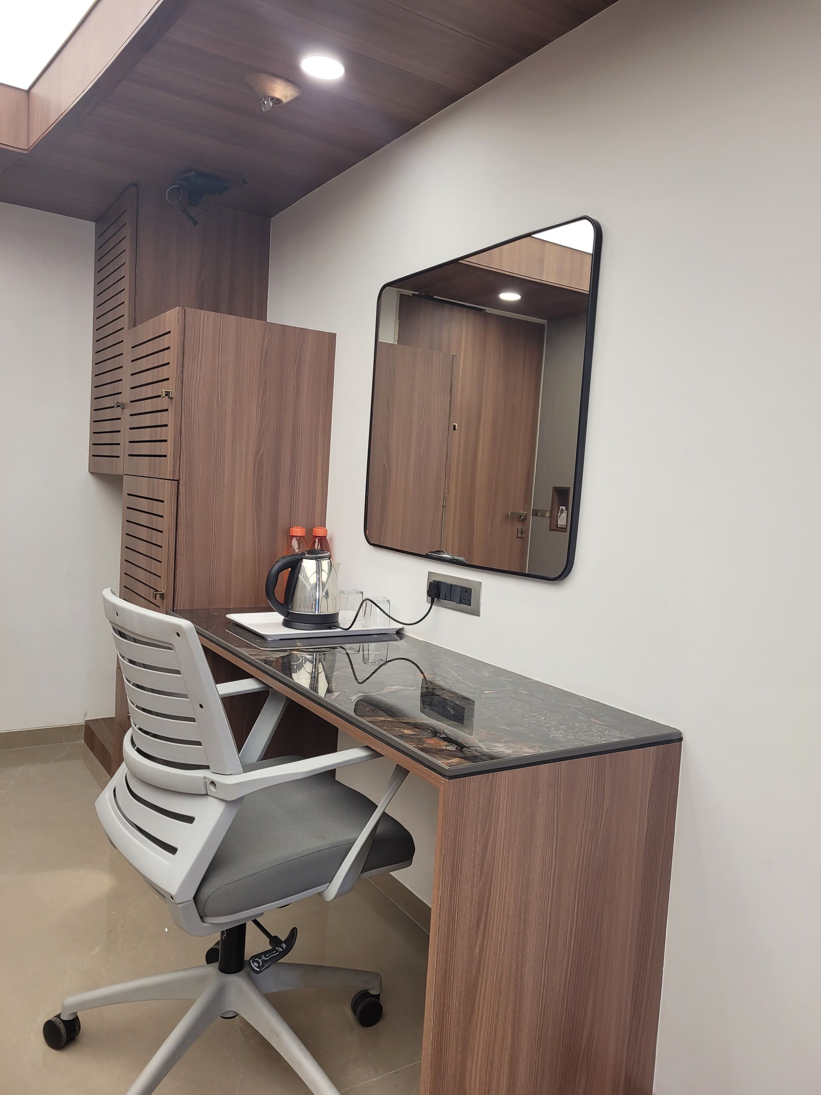 Un espacio de oficina moderno con un escritorio de madera, una silla de oficina blanca, un espejo y una lámpara en el techo.