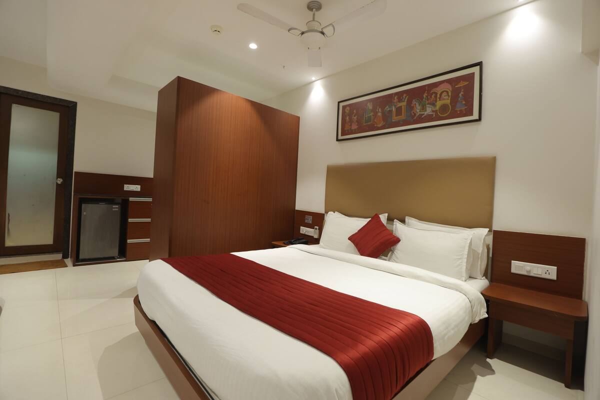 A hotel room with a large bed, a wooden wardrobe, a small desk, and a ceiling fan.