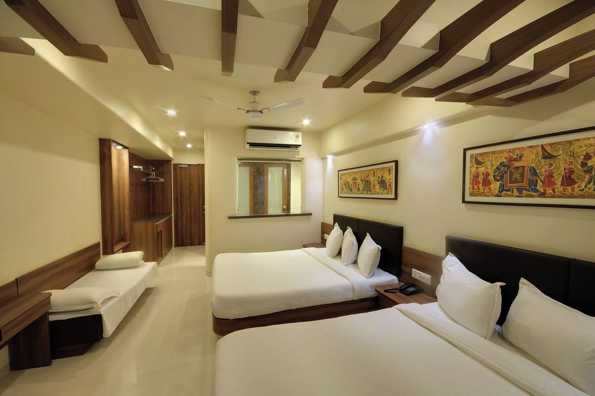 A hotel room with two beds, wooden headboards, a ceiling fan, an air conditioning unit, a small window, and a wall-mounted painting.
