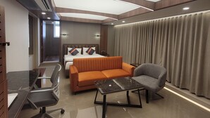 A modern hotel room with a bed, orange sofa, grey armchair, and a glass table. - Hotel Shreeji Vatika-Airport Road (Surat)