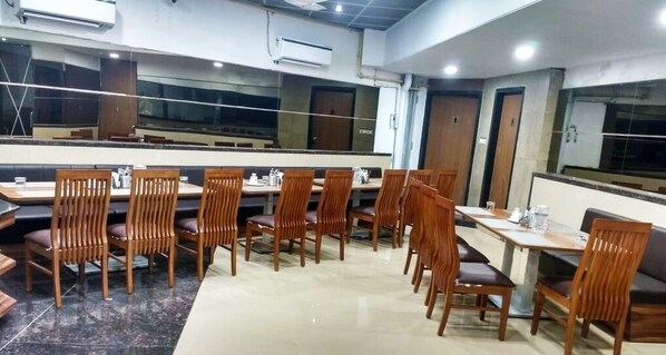 A dining area with wooden chairs and tables, air conditioning units, and a large mirror on the wall.