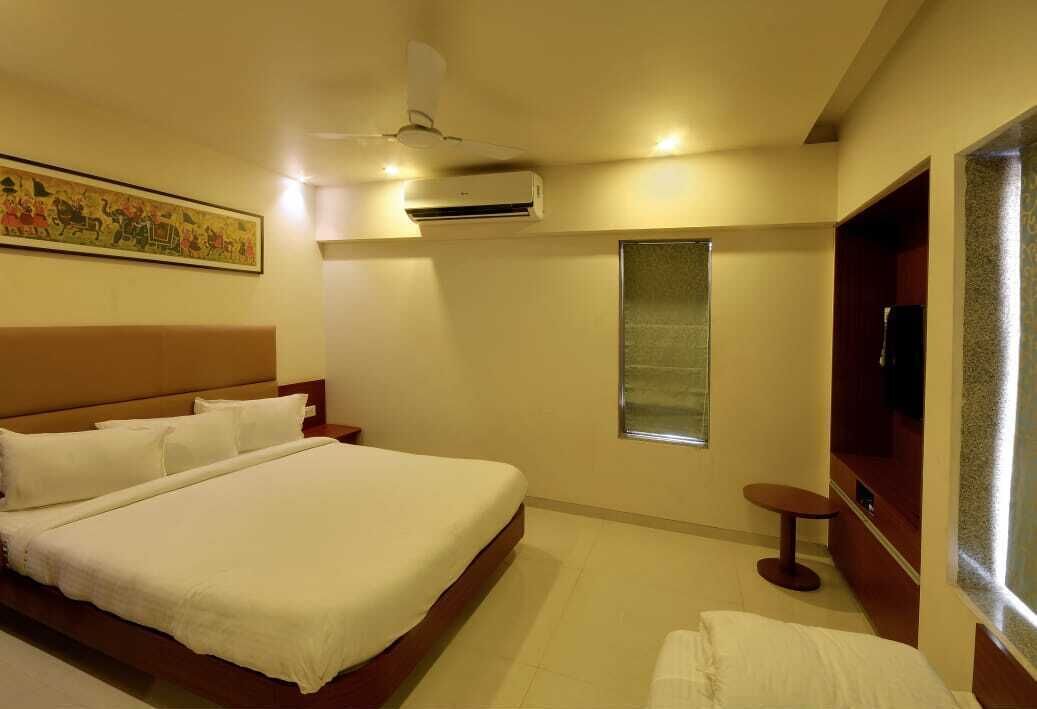 A hotel room with a large bed, a small table, a TV, and an air conditioning unit.