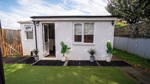 Una casa pequeña de un solo piso con fachada blanca, una puerta principal y dos ventanas. Hay tres macetas con plantas frente a las ventanas.