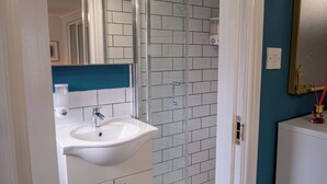 Un baño con un lavamanos blanco, cabina de ducha con mampara de vidrio y pared de acento azul.
