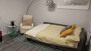Un dormitorio moderno con cama, una silla, una lámpara y una mesita con una planta.
