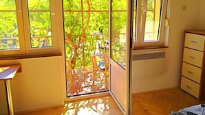 Ein Zimmer mit einer Glastür zu einem Balkon, einem kleinen Fenster, einem Heizkörper und Holzboden.