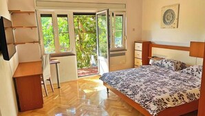 Ein Schlafzimmer mit Bett, Schreibtisch und Stuhl. Ein Fenster bietet Blick ins Grüne.