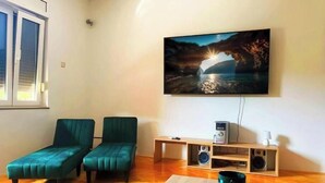 Ein Wohnzimmer mit Holzboden, zwei grünen Sofas, einem Couchtisch, einem an der Wand befestigten Fernseher und einer Holz-Unterhaltungseinheit mit Lautsprechern.