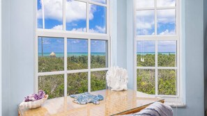 A room with a large window overlooking a beach and a thatched structure. - Marina & Ocean | Corner Unit | Ocean Pointe 4201 (Tavernier)
