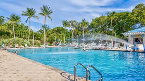 A swimming pool with lounge chairs and umbrellas, surrounded by palm trees and a water feature. - Marina & Ocean | Corner Unit | Ocean Pointe 4201 (Tavernier)