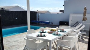 An outdoor patio with a pool, white furniture, and a table set with plates and cups. - Villa Anny, heated pool, ideal for families! (PLAYA BLANCA)