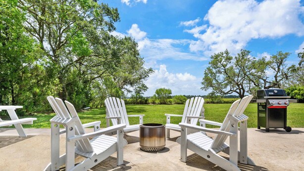 A patio area with Adirondack chairs, a metal fire pit, and a grill. - Water Views, Minutes to Downtown & Folly Beach! (Charleston)