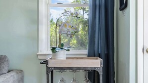 A room with a window, a metal cart with wine glasses, a gray couch, and a door. - Water Views, Minutes to Downtown & Folly Beach! (Charleston)