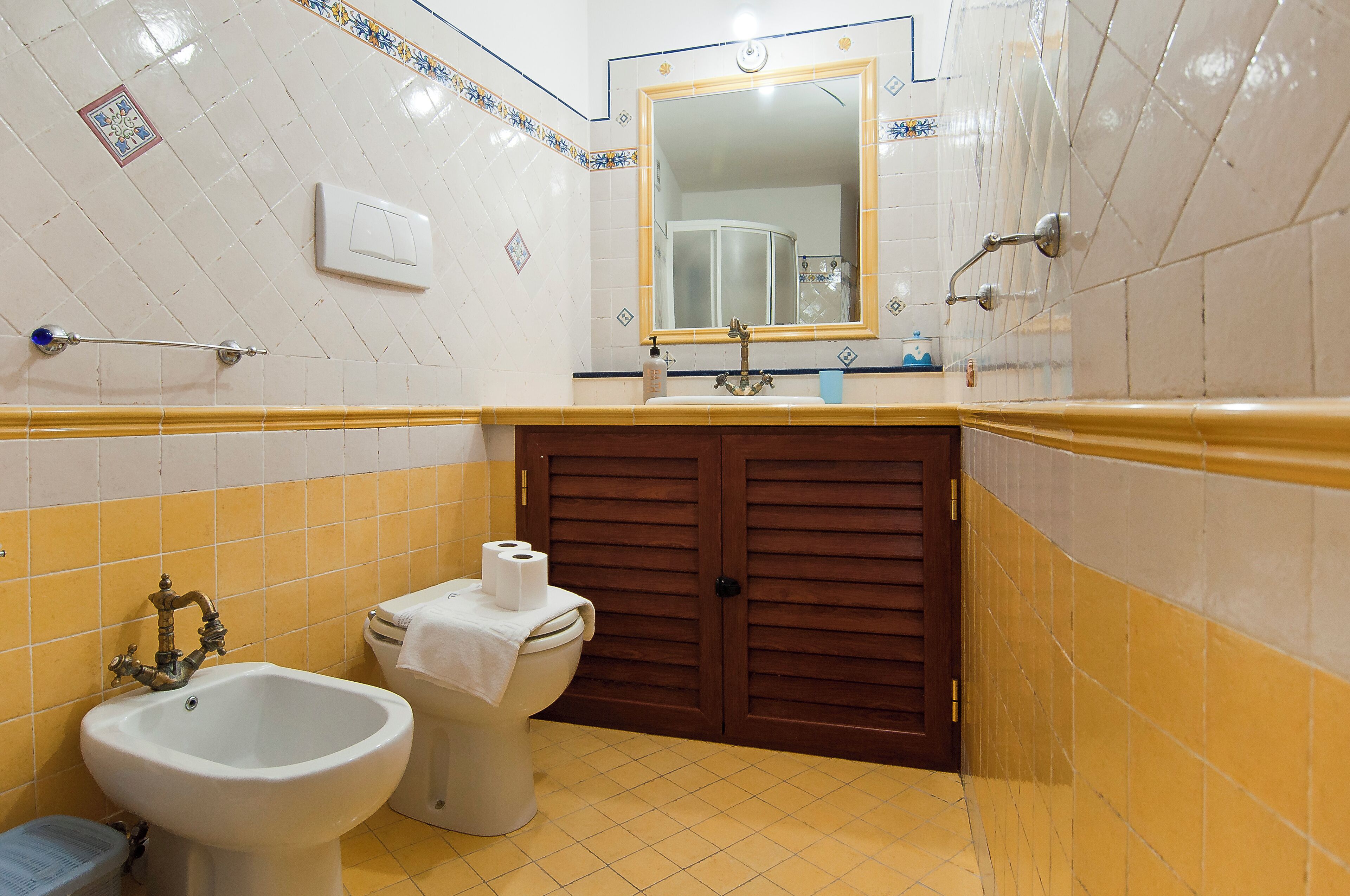 A bathroom with a bidet, toilet, sink, mirror, and wooden door.
