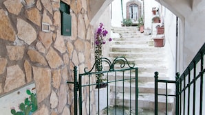A stone staircase with a metal gate, potted plants, and a view of a building in the background. - Casa Vacanza Opuntia (Sperlonga)