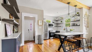 A modern kitchen with wooden flooring, a central island with stools, white cabinets, and a built-in oven.