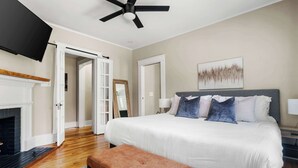 A bedroom with a large bed, a ceiling fan, a fireplace, and a door leading to another room.
