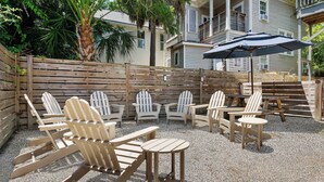 A patio area with Adirondack chairs and tables, a wooden fence, and a building in the background.