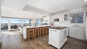 Cocina moderna con una isla grande, armarios blancos y vista a la playa.