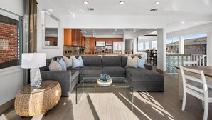 A modern living room with a sectional sofa, a glass coffee table, and a woven side table. - Oceanfront Home with Stunning Balcony Views (Newport Beach)