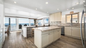 A modern kitchen with a large island, wooden flooring, and a view of the ocean. - 5-Bedroom Oceanfront Escape with Private Balcony (Newport Beach)