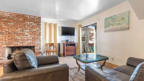 A living room with leather sofas, a glass coffee table, a brick fireplace, and a flat-screen TV mounted on the wall. - Cozy 2-Bedroom Getaway (Newport Beach)