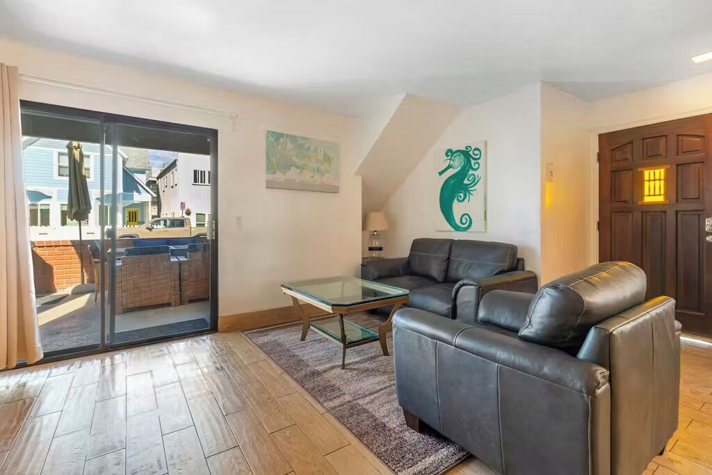 A living room with a glass coffee table, a leather sofa, and a sliding glass door leading to an outdoor area.