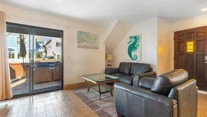 A living room with a glass coffee table, a leather sofa, and a sliding glass door leading to an outdoor area. - Cozy 2-Bedroom Getaway (Newport Beach)