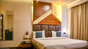 A hotel room with a large bed, a wooden headboard, a nightstand, a mirror, and a window with curtains. - Hotel Leosh Lansdwone (Lansdowne)