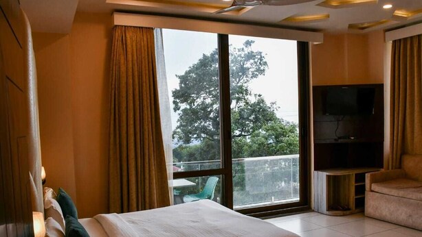 A hotel room with a large bed, a TV, and a balcony with a view of trees. - Hotel Leosh Lansdwone (Lansdowne)