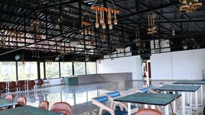 A spacious indoor area with tables and chairs, large windows, and a high ceiling with hanging lights. - Hotel Leosh Lansdwone (Lansdowne)