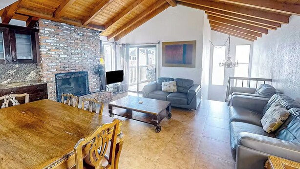 A spacious living room with a stone fireplace, a wooden dining table, and leather sofas. - Seaside Getaway Just Steps from the Ocean (Newport Beach)