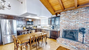 A modern kitchen with stainless steel appliances, a wooden dining table, and a brick fireplace. - Seaside Getaway Just Steps from the Ocean (Newport Beach)
