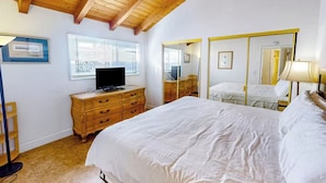 A bedroom with a wooden ceiling, a bed, a dresser, a mirror, and a television. - Seaside Getaway Just Steps from the Ocean (Newport Beach)