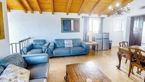 A living room with a wooden ceiling, a blue sofa, a wooden coffee table, and a dining area with a wooden table and chairs. - Seaside Getaway Just Steps from the Ocean (Newport Beach)