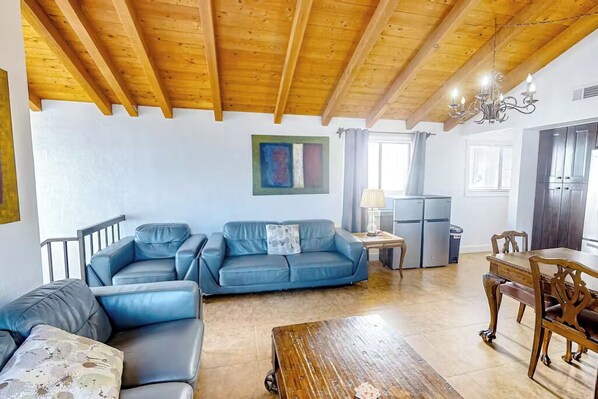 A living room with a wooden ceiling, a blue sofa, a wooden coffee table, and a dining area with a wooden table and chairs.