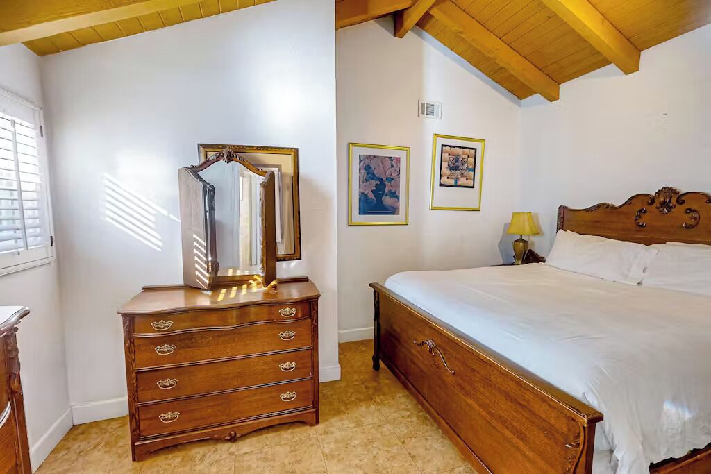 A bedroom with a wooden dresser, a bed with white linens, and two framed pictures on the wall.