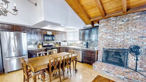 A modern kitchen with stainless steel appliances, a wooden dining table, and a brick fireplace. - Coastal Duplex Home Steps from the Beach (Newport Beach)